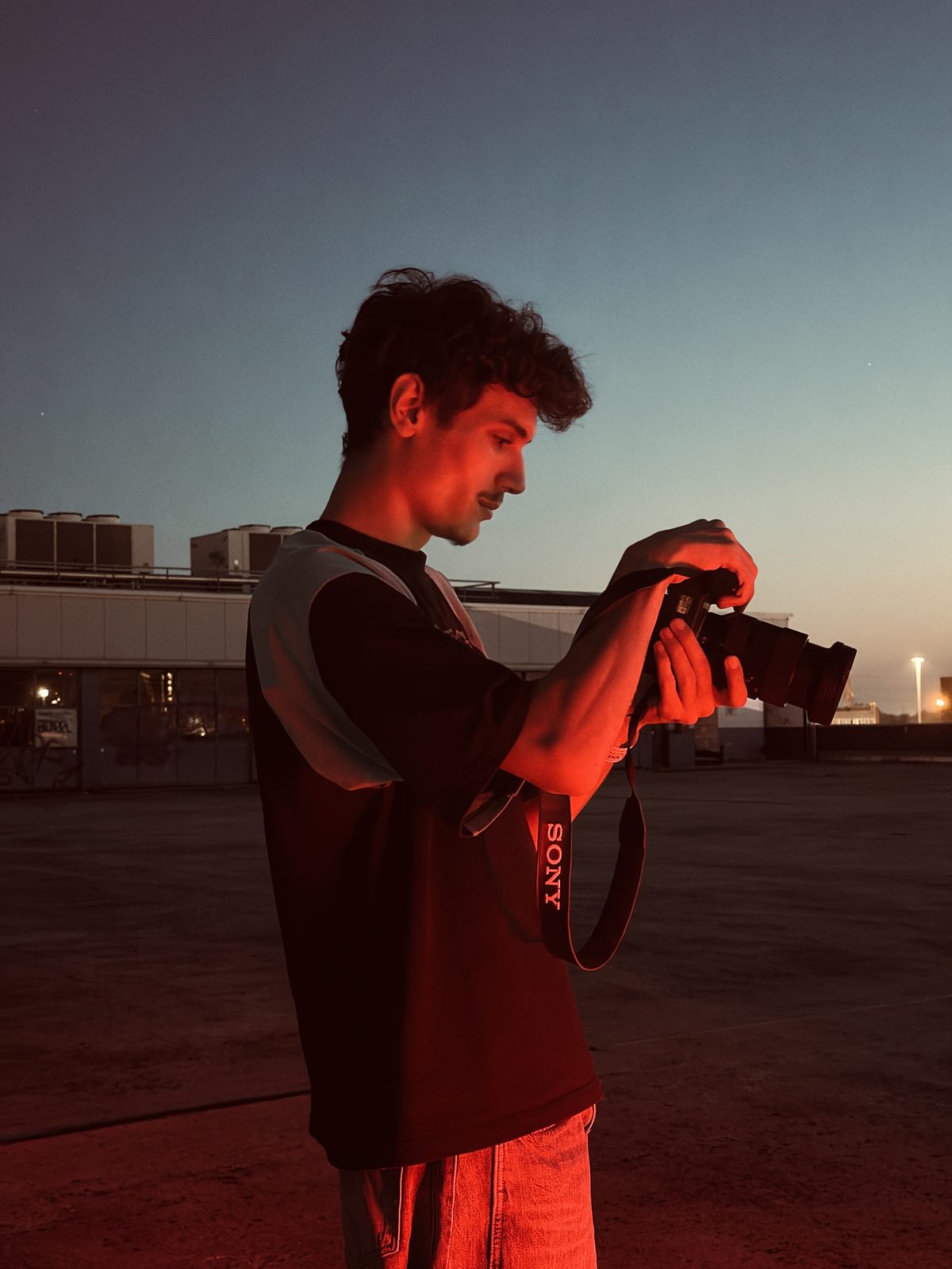 Tommaso Generoso checking a shot on a Sony camera at dusk, lit by red light on an empty rooftop