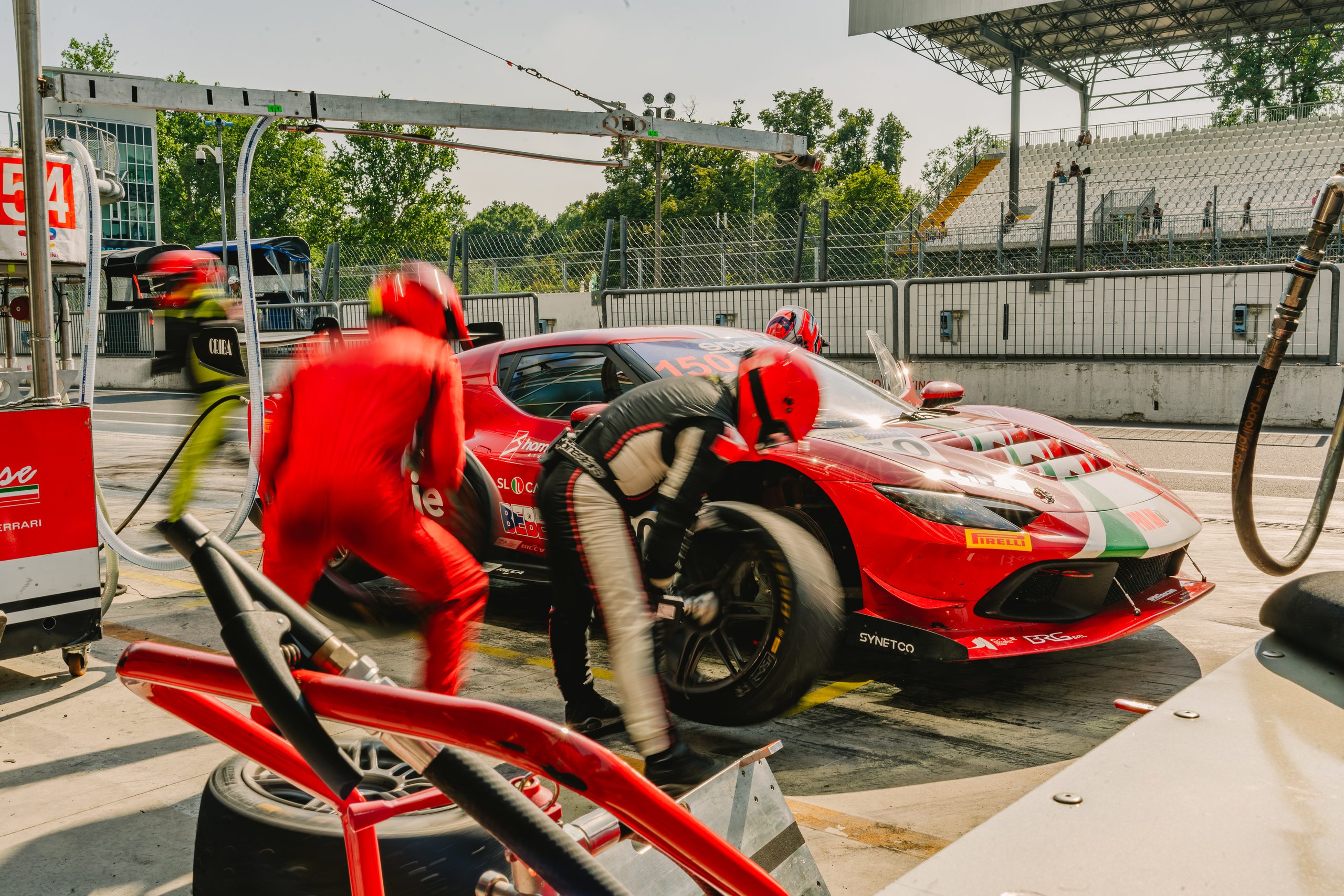 Mechanics in red overalls and helmets blur around a red Ferrari, number 150, as a wheel comes off during a pit stop
