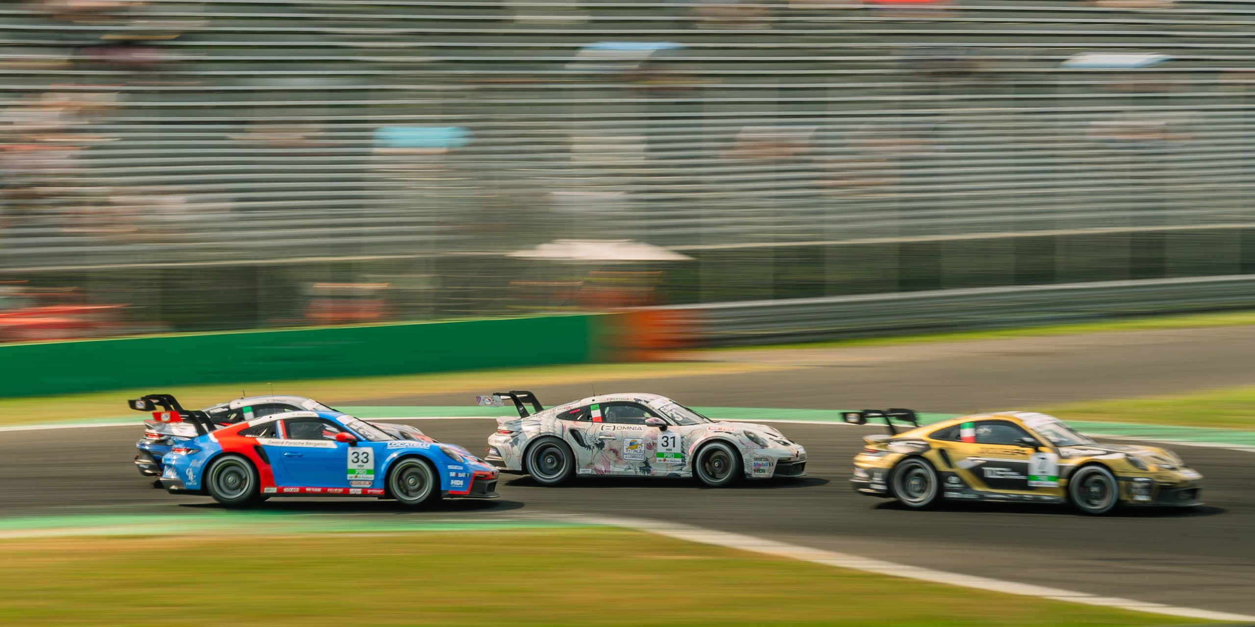 A pack of Porsche 911 GT3 Cup cars, numbers 33 and 31 leading, panned through a corner with the grandstand streaked behind