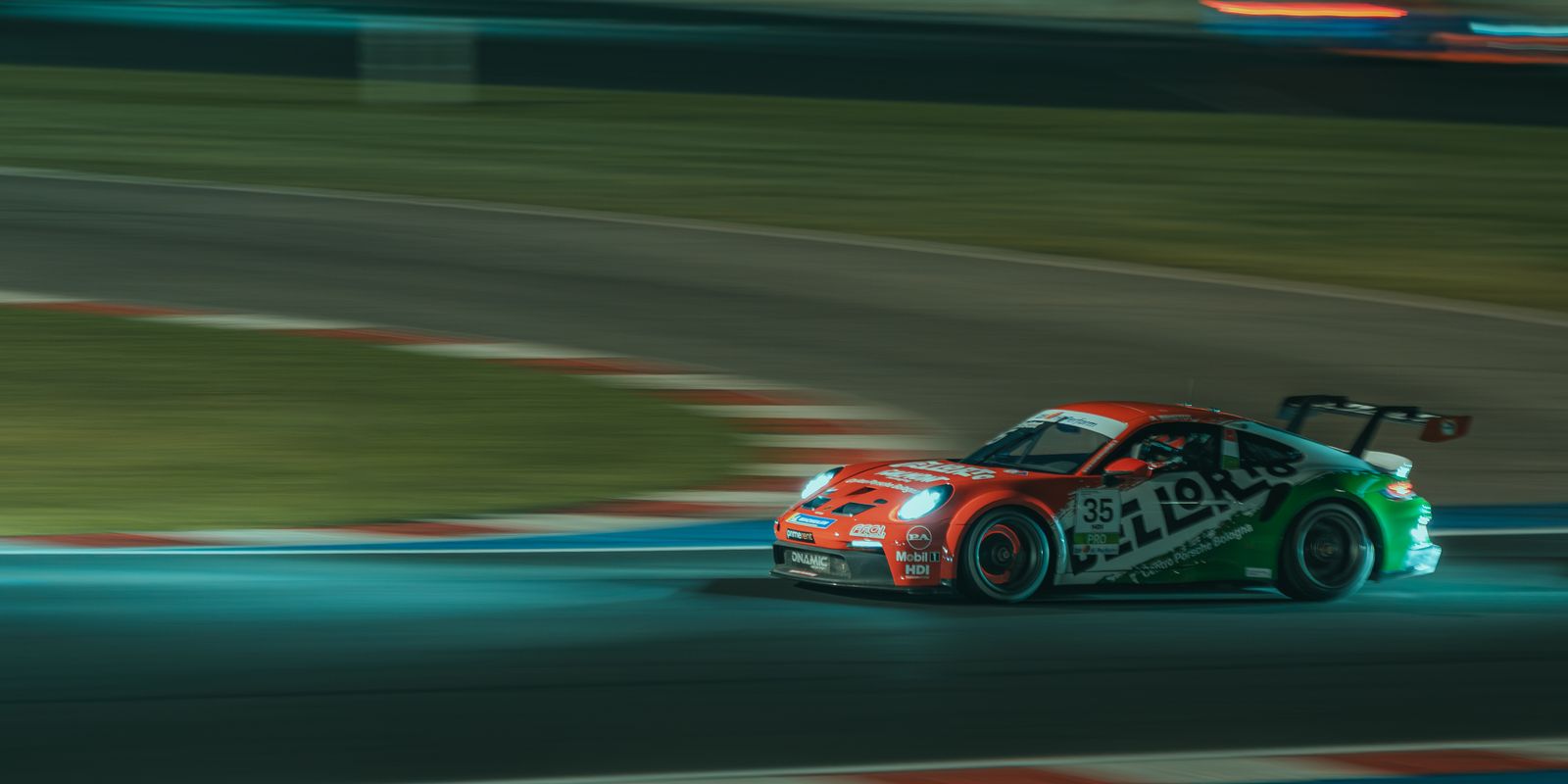 A red and green Porsche 911 GT3 Cup, number 35, with headlights on, panned through a corner at night