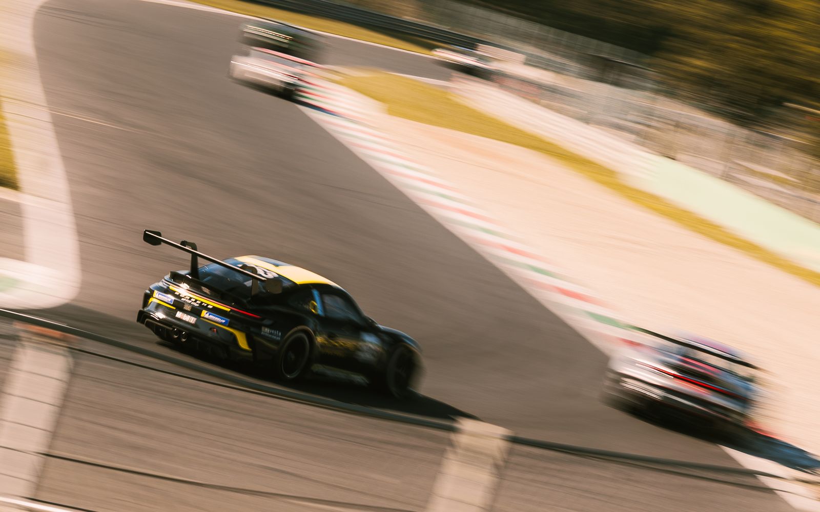 A black and yellow Porsche 911 GT3 Cup seen from behind through a chicane, other cars blurred ahead and beside it