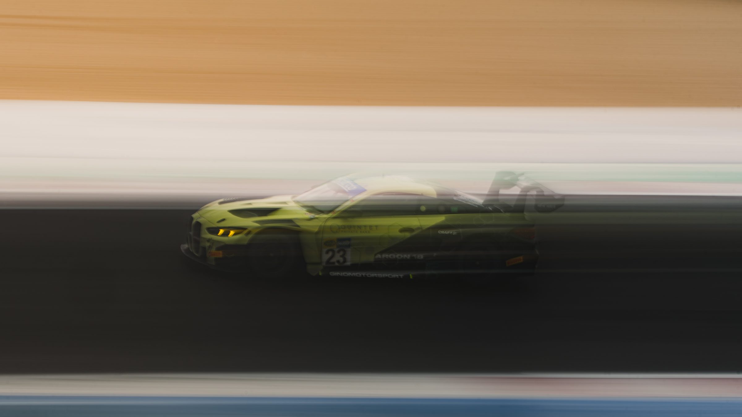 A green BMW M4 GT3, number 23, panned at a fifth of a second so the track and kerbs dissolve into bands of colour