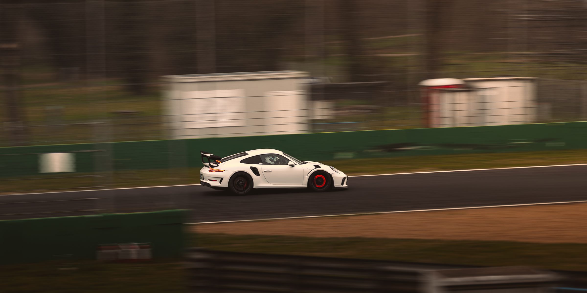 A white Porsche 911 GT3 RS panned at speed along a circuit, the barriers and trees streaked behind it